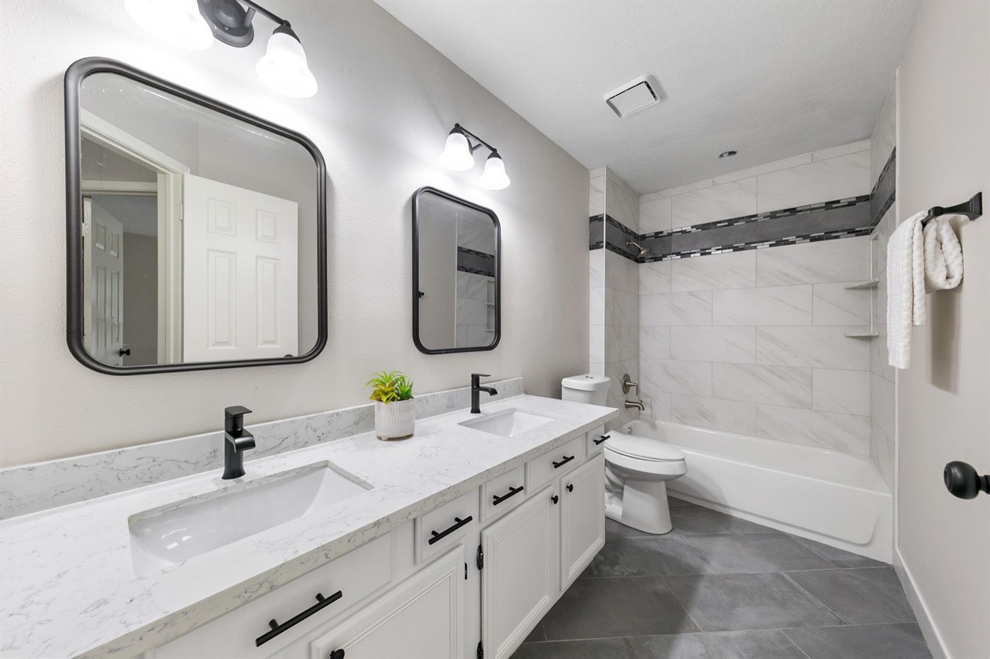 Bathroom renovation with dual vanity, black fixtures, and marble-look tub surround