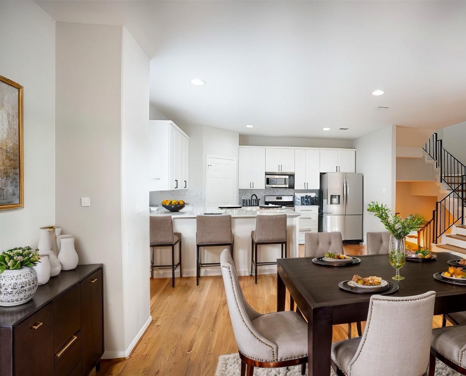 Open dining room and white kitchen with peninsula seating and warm wood flooring