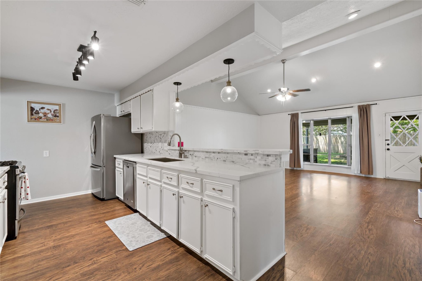 Updated white kitchen with stone-look counters, backsplash, pendant lighting, and open living area