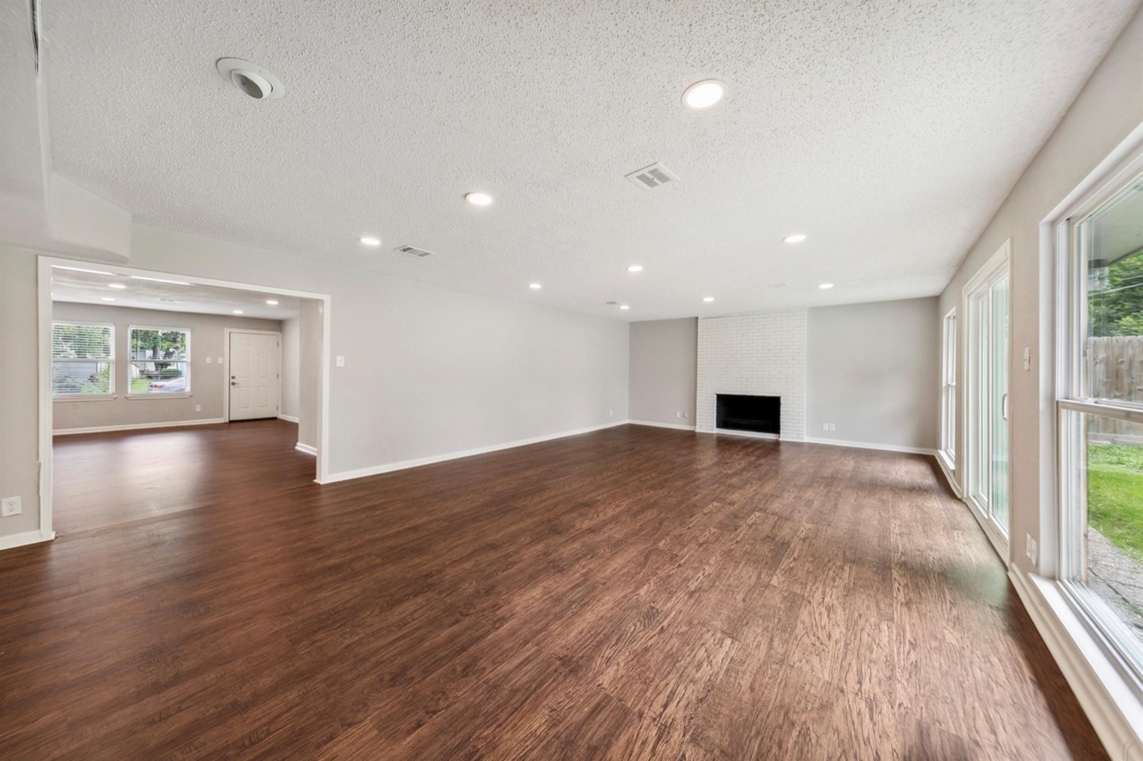 Refreshed open living area with wood-look flooring, recessed lighting, and white brick fireplace