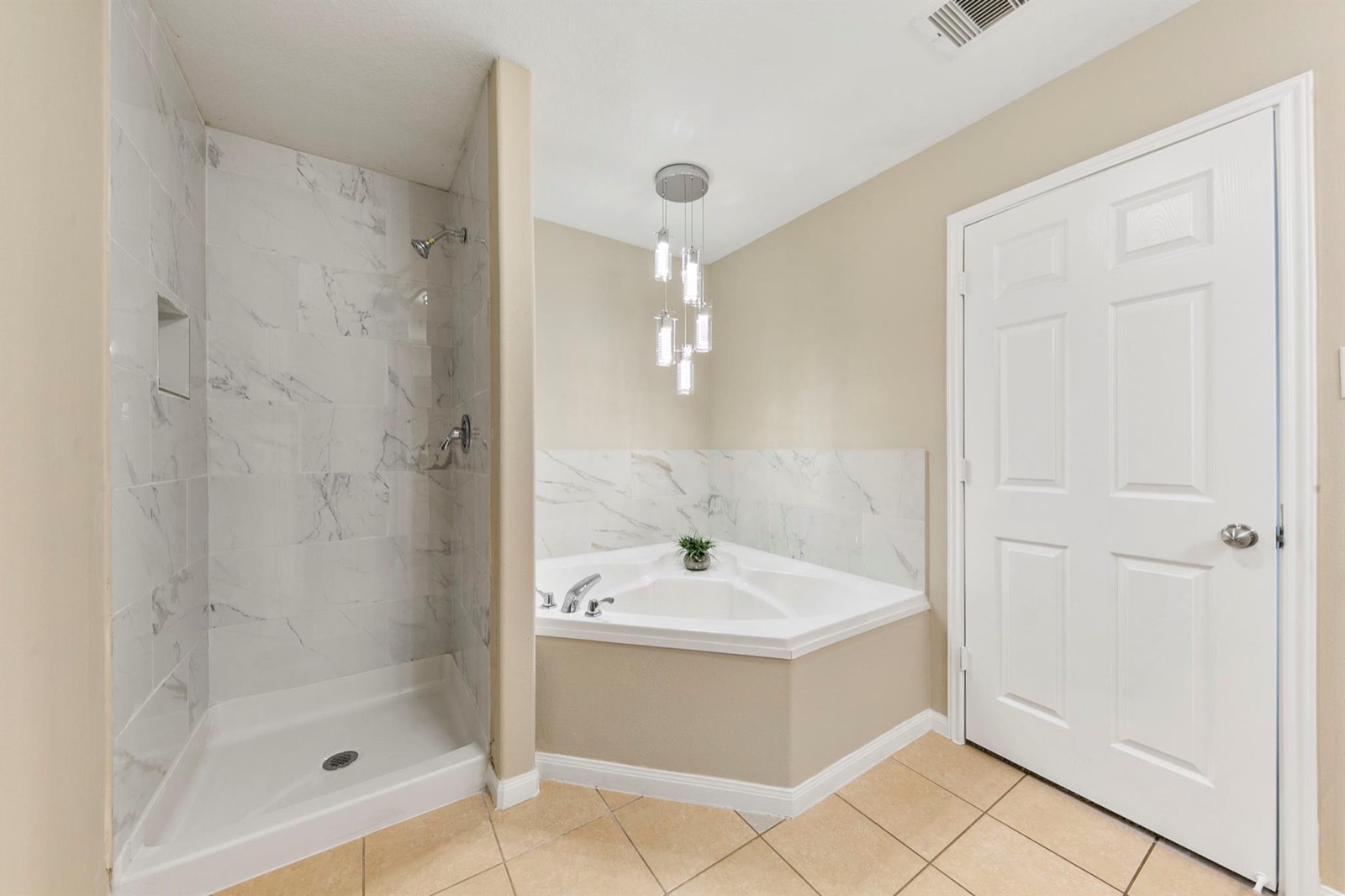 Updated primary bathroom with marble-look tiled shower, corner soaking tub, and modern pendant lighting