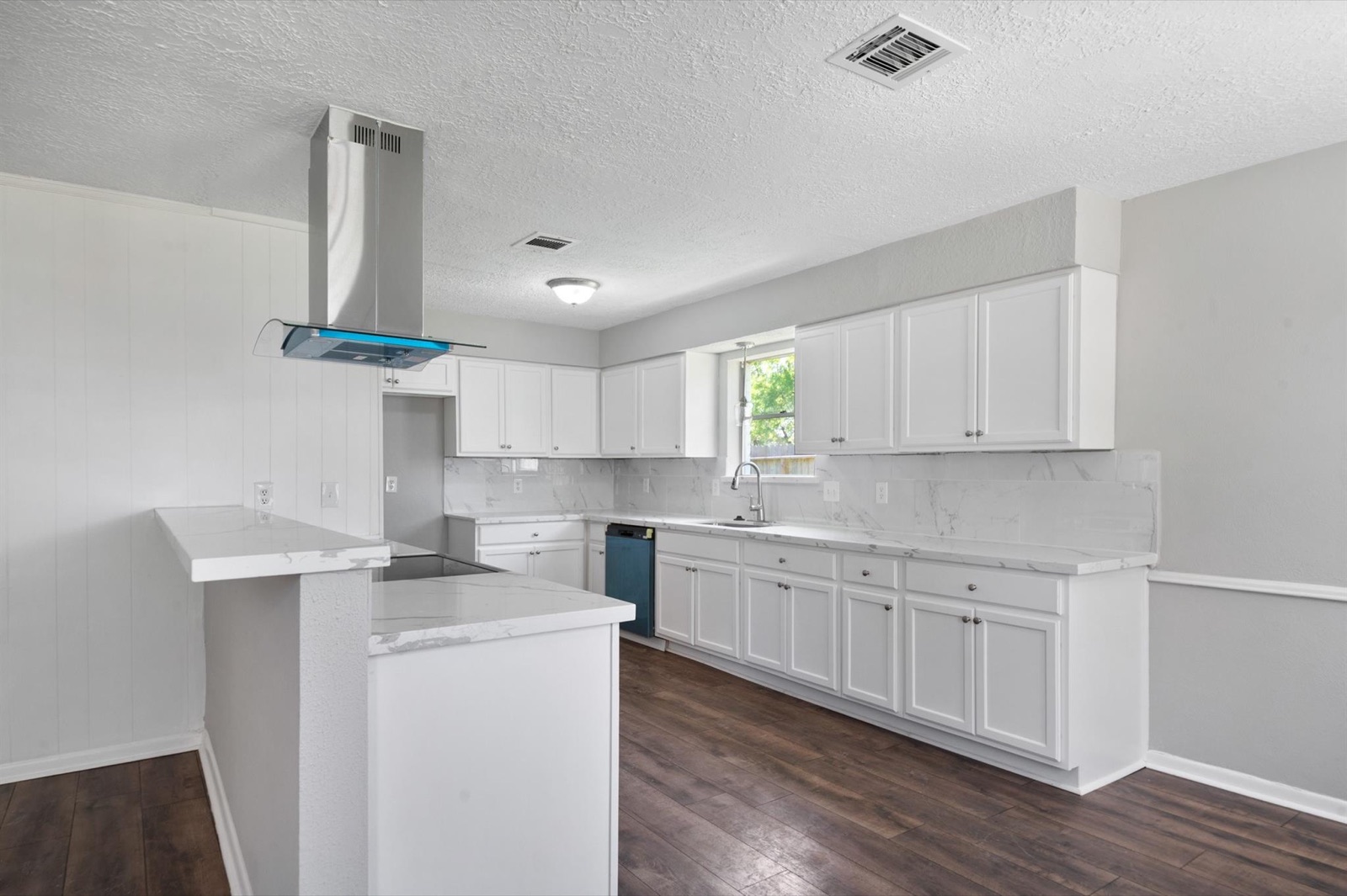 Completed white kitchen with stone-look counters, matching backsplash, and island range hood